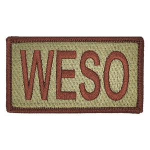 May include: A tan rectangular patch with a brown embroidered border and the word "WESO" in brown lettering.
