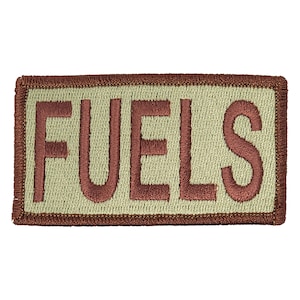 May include: A brown embroidered patch with the word "FUELS" in white lettering on a beige background.