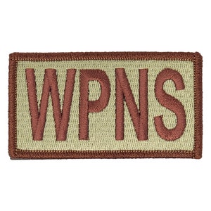 May include: A tan rectangular patch with a brown embroidered border and the word "WPNS" in brown lettering.
