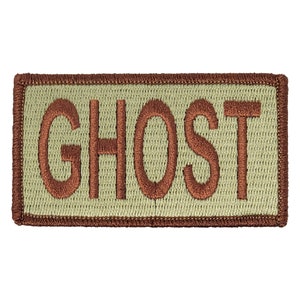 May include: A tan rectangular patch with brown embroidered text that reads "GHOST".