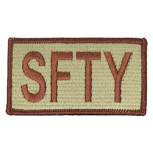 May include: A tan rectangular patch with a brown border and the word "SFTY" embroidered in brown.