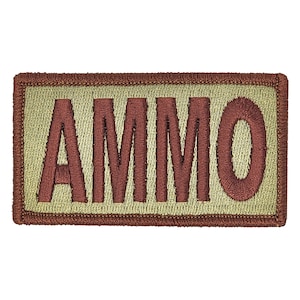 May include: A tan rectangular patch with a brown embroidered border and the word "AMMO" in brown lettering.