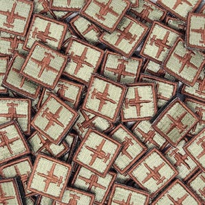 Könnte beinhalten: Nahaufnahme eines Stapels kleiner, quadratischer Patches mit einem braunen gestickten Bild eines Flugzeugs auf hellgrünem Hintergrund.