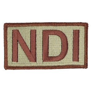 Könnte beinhalten: Ein beigefarbener gestickter Aufnäher mit den Buchstaben "NDI" in Braun.