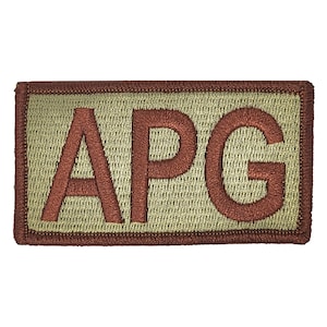 May include: A tan rectangular patch with a brown embroidered border and the letters "APG" in brown.