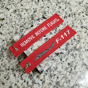 May include: Two red keychains with white text. One keychain says "REMOVE BEFORE FLIGHT" and the other says "F-117".