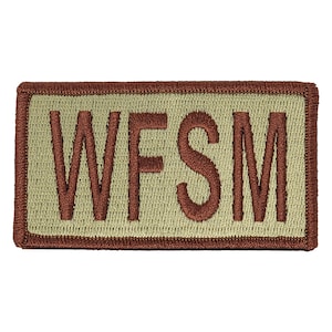 May include: A tan embroidered patch with a brown border. The patch says "WFSM" in brown lettering.