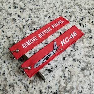 May include: Red airplane keychain with a white airplane silhouette and the text "REMOVE BEFORE FLIGHT" and "KC-46".