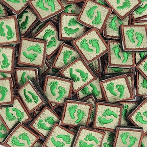 May include: A close-up image of a collection of small, square patches with a brown border and a green footprint design. The patches are arranged in a random pattern, creating a textured background.
