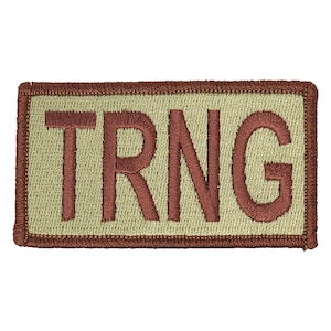 May include: A tan rectangular patch with a brown border and the word "TRNG" embroidered in brown.