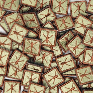 Könnte beinhalten: Ein Stapel grüner und brauner gestickter Patches mit einem Hubschrauber-Design. Die Patches sind quadratisch und haben einen braunen Rand.