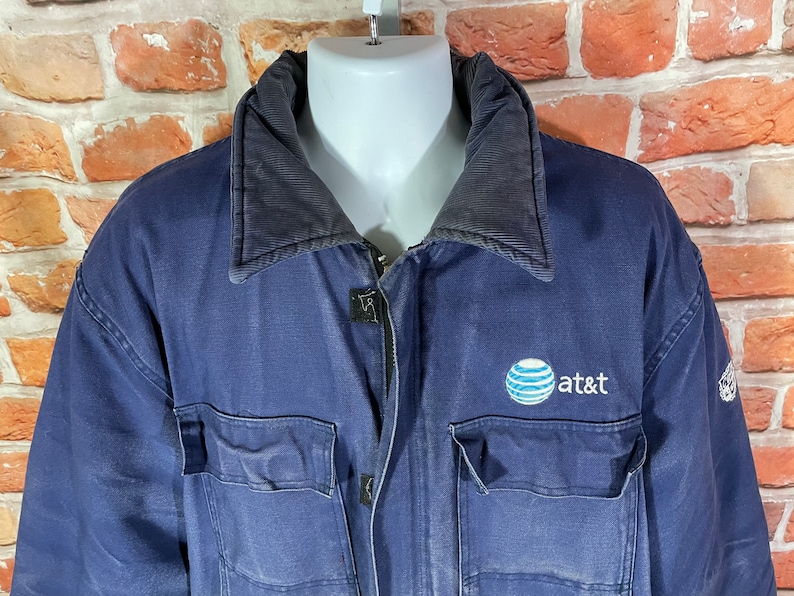 May include: A navy blue work jacket with a black corduroy collar and a large embroidered AT&T logo on the chest.