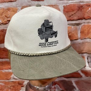May include: A white and gray baseball cap with a curved brim. The cap features a graphic of a lawn mower and the text "DIXIE CHOPPER. The World's Fastest Lawn Mower."