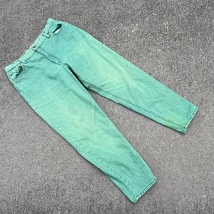 May include: A pair of light green denim jeans. The jeans have a classic five-pocket design, a button and zipper closure, and belt loops. The denim has a faded, slightly worn appearance.