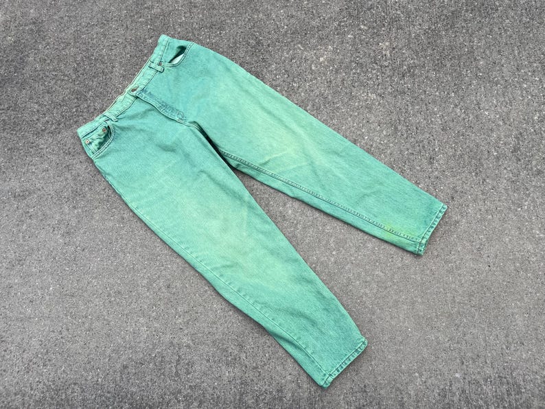 May include: A pair of light green denim jeans. The jeans have a classic five-pocket design, a button and zipper closure, and belt loops. The denim has a faded, slightly worn appearance.