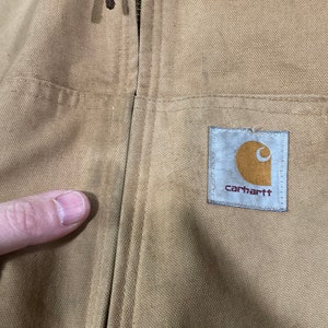 May include: A tan Carhartt work jacket with a zipper closure and a Carhartt logo patch on the chest.