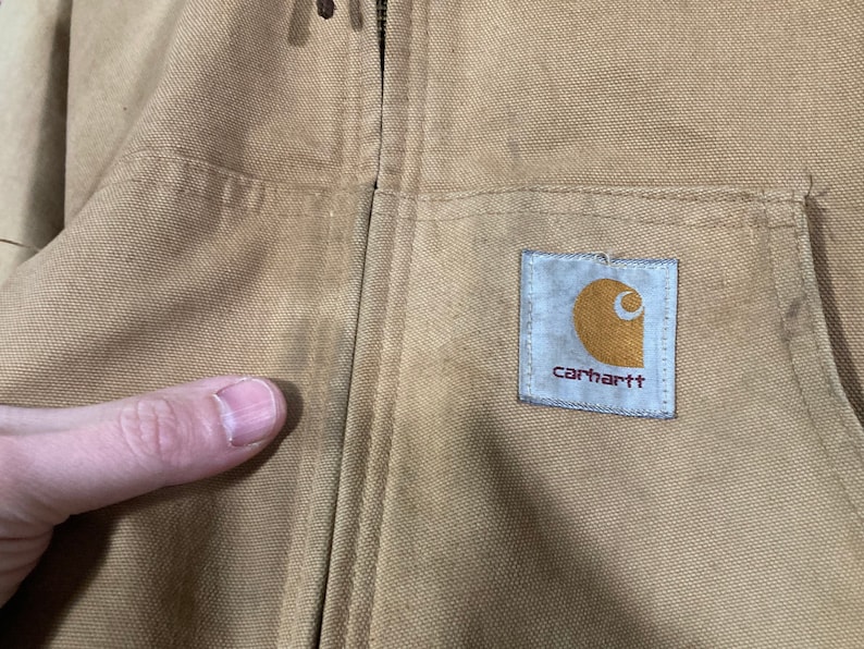 May include: A tan Carhartt work jacket with a zipper closure and a Carhartt logo patch on the chest.