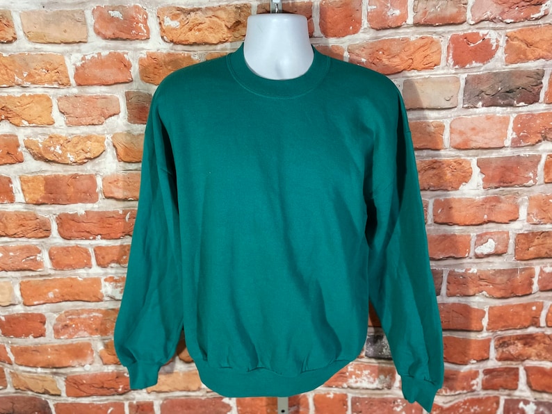May include: A plain, dark green sweatshirt with long sleeves and a crew neck.