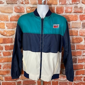 Op de afbeelding: Een windjack in de kleuren blauw, wit en turquoise met een ritssluiting en een Pepsi-logo op de borst.