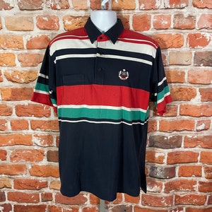 May include: A striped short-sleeved polo shirt with a red, white, green, and blue color scheme. The shirt has a small embroidered logo on the chest.