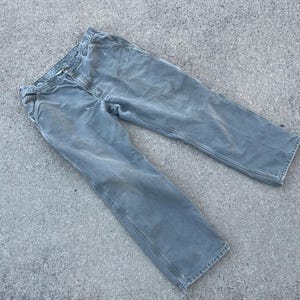 Puede incluir: Un par de pantalones de trabajo grises con un aspecto descolorido. Los pantalones tienen una pierna recta y est&aacute;n hechos de una tela duradera.