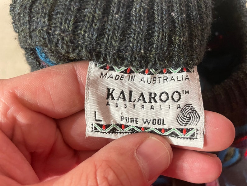 May include: A close-up of a gray wool sweater tag with the text "Made in Australia", "KALAROO&trade; AUSTRALIA", "PURE WOOL" and a size "L" label.