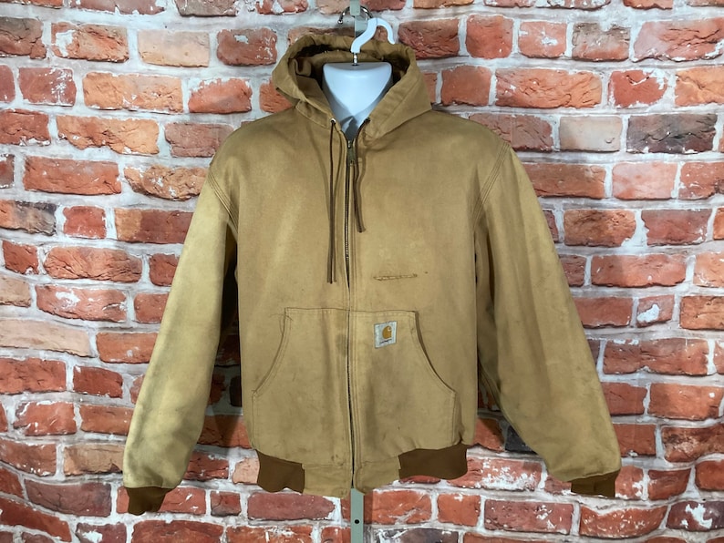 May include: A brown hooded work jacket with a zipper closure and a Carhartt logo patch on the chest. The jacket has a brown ribbed knit collar, cuffs, and waistband.