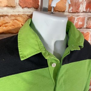 May include: A green and black rugby shirt with a button-up collar. The shirt has a contrasting color block design.