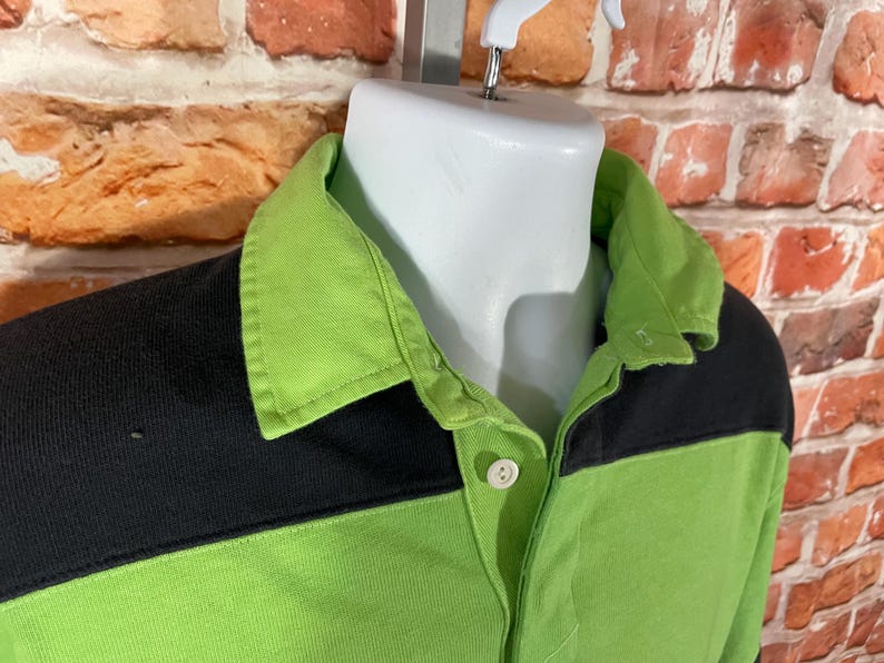 May include: A green and black rugby shirt with a button-up collar. The shirt has a contrasting color block design.