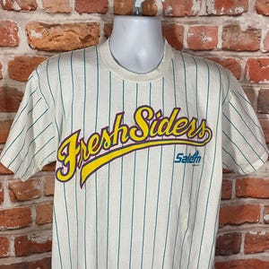 May include: White striped baseball jersey with the text "Fresh Siders" in yellow, purple, and blue lettering. The text "Salem" is printed in blue below the main text.