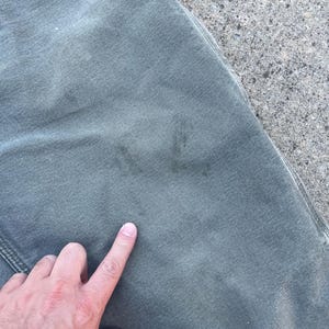 Puede incluir: Un pantal&oacute;n cargo verde con una marca descolorida en la parte delantera. La marca parece ser una letra o un s&iacute;mbolo.