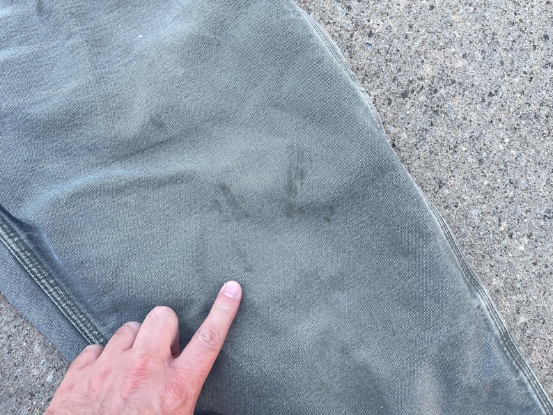 Puede incluir: Un pantal&oacute;n cargo verde con una marca descolorida en la parte delantera. La marca parece ser una letra o un s&iacute;mbolo.