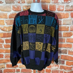 May include: A black sweater with a colorful, geometric pattern. The design features squares in shades of blue, purple, gold, and red, each containing unique abstract shapes. The sweater has long sleeves and a crew neck.