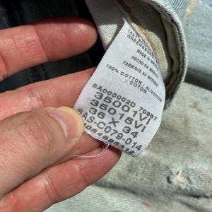 Peut inclure: Gros plan sur une &eacute;tiquette blanche avec du texte noir, sur un fond en denim bleu clair. L'&eacute;tiquette comprend le texte "100% COTON" et les mesures "36 X 34". L'&eacute;tiquette comprend &eacute;galement le texte "MADE IN MEXICO".