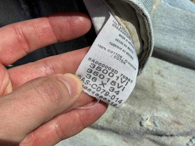 Peut inclure: Gros plan sur une &eacute;tiquette blanche avec du texte noir, sur un fond en denim bleu clair. L'&eacute;tiquette comprend le texte "100% COTON" et les mesures "36 X 34". L'&eacute;tiquette comprend &eacute;galement le texte "MADE IN MEXICO".
