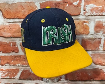 May include: A navy blue and gold baseball cap with the word "IRISH" embroidered in green letters.