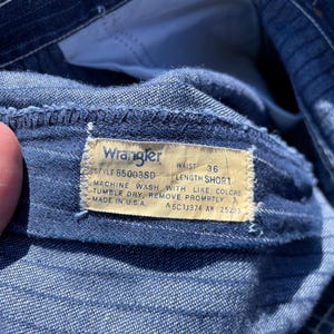 May include: Close-up of blue denim shorts with a Wrangler tag. The tag reads "WAIST 36 LENGTH SHORT" and includes washing instructions. The shorts are made in the U.S.A.