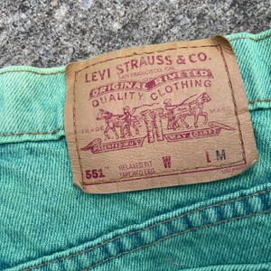 May include: Close-up of a section of turquoise denim jeans. A rectangular brown leather patch with the Levi Strauss & Co. logo is sewn onto the jeans. The patch includes text and a graphic of people and horses.