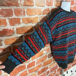 May include: A colorful, striped sweater with a geometric pattern in shades of blue, red, green, and black. The sweater has a crew neck and long sleeves.
