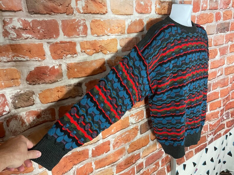 May include: A colorful, striped sweater with a geometric pattern in shades of blue, red, green, and black. The sweater has a crew neck and long sleeves.