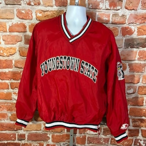 May include: Red nylon pullover jacket with a V-neck collar, featuring the text "YOUNGSTOWN STATE" in green and white. The jacket has white and black striped trim on the collar, cuffs, and hem. A penguin logo is on the right sleeve.