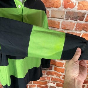 May include: A long-sleeved shirt with black and green horizontal stripes. The shirt has a button-up collar and a button closure.