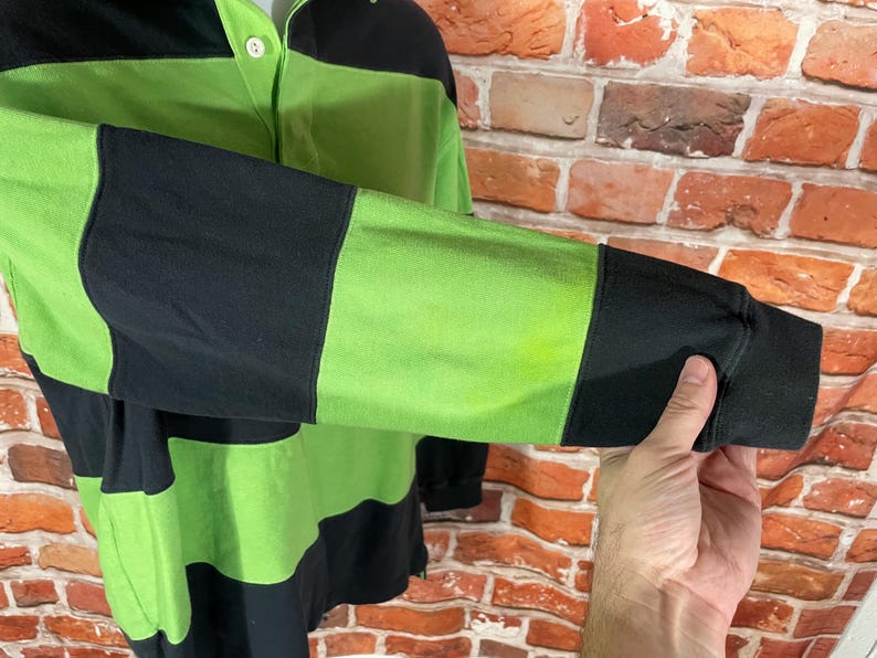May include: A long-sleeved shirt with black and green horizontal stripes. The shirt has a button-up collar and a button closure.