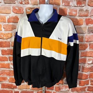 May include: A white ceramic mug with a black handle and the text "But First, Coffee" in a bold, black font. The mug is set against a blurred background, suggesting a cozy setting.