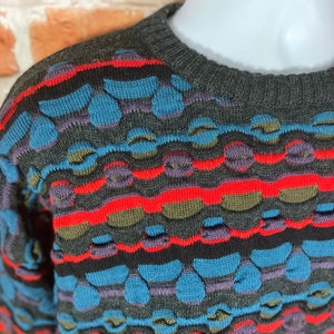 May include: A gray, blue, red, and green patterned sweater with a crew neck.