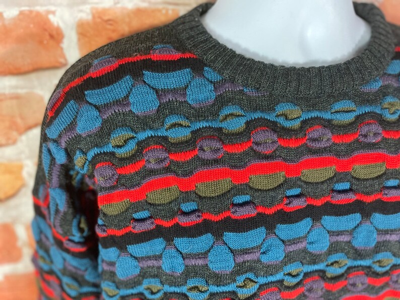 May include: A gray, blue, red, and green patterned sweater with a crew neck.