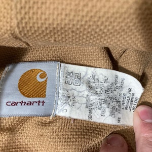 May include: A brown Carhartt workwear jacket with a white tag that reads "Must 40 Separately to not bleach Tumble dry low Remove promptly from dryer Only 100% Cotton 100% Polyester GG Shell Lining See care instructions", and a brown tag that reads "Large Regular Josern JR106".