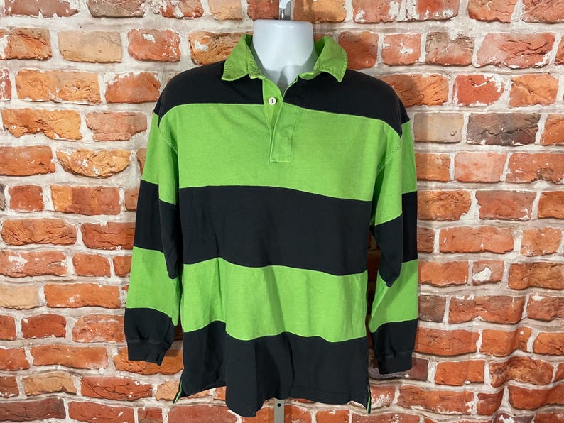 May include: A long-sleeved rugby shirt with black and green horizontal stripes. The shirt has a button-up collar and a button placket.