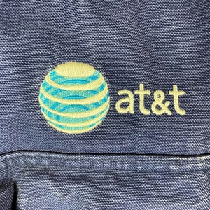 May include: A blue canvas bag with an embroidered AT&T logo. The logo features a blue and yellow globe with a white outline.