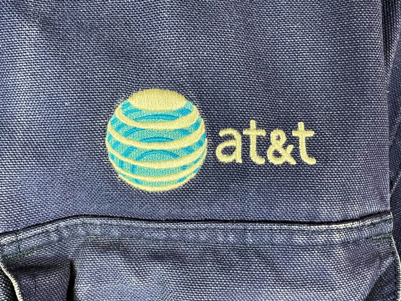 May include: A blue canvas bag with an embroidered AT&T logo. The logo features a blue and yellow globe with a white outline.